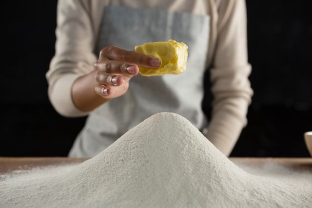 Mid section of woman adding butter cube into flour