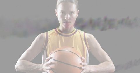 Female basketball player holding ball facing camera showing focus and fierce determination