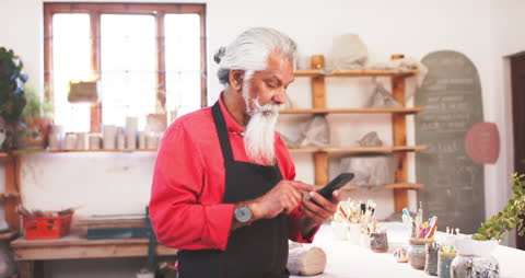 Experienced Potter with Beard Engaging with Smartphone in Artisan Studio