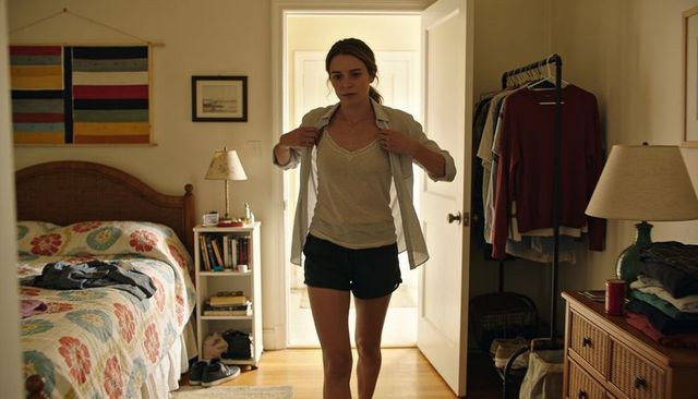 Adjusting light shirt in cozy bedroom, woman wearing camisole and shorts by wardrobe