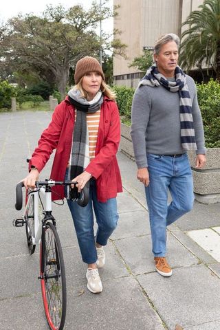 Mature couple walking with bicycle on city sidewalk wearing scarves and autumn jackets