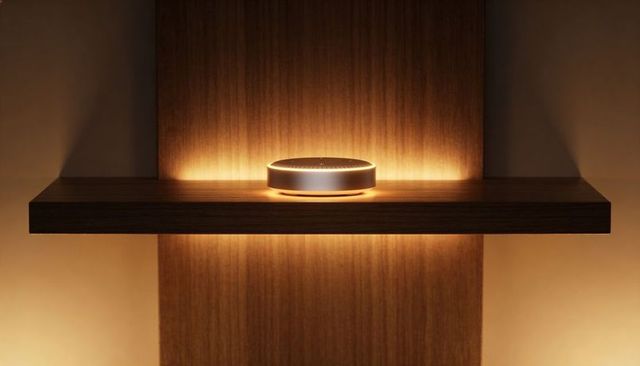 Minimalist smart speaker glowing on floating wood shelf with warm amber halo