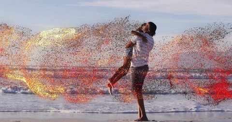 Father lifting daughter on beach at golden hour with swirling colorful spark particles