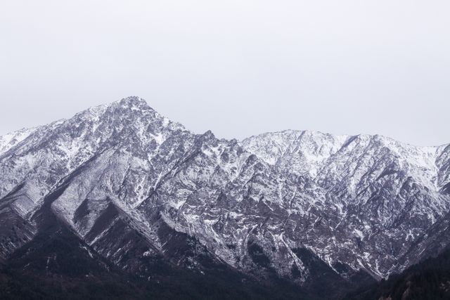 This image showcases the towering, snow-capped peaks of a rocky mountain range under a cloudy sky. The rugged terrain and wintry landscape evoke feelings of adventure and the majesty of nature. Ideal for travel and outdoor adventure content, this image can be used in blogs, websites, advertisements, and posters promoting tourism, hiking, and scenic beauty.