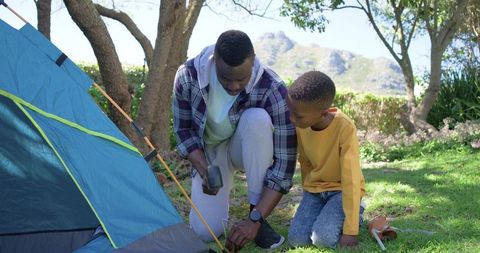 African american father and son setting up blue tent camping outdoors family bonding