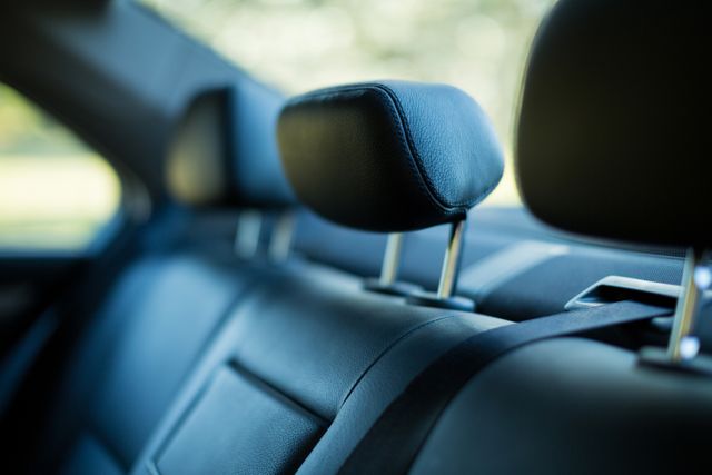 Close up of leather back seats in a car, showcasing the headrest and seatbelt. Ideal for use in automotive advertisements, car reviews, luxury vehicle promotions, or articles about car interiors and comfort.