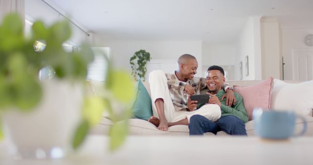 Shows an African American couple enjoying leisure time together on a comfy sofa, sharing moments while using a tablet. Perfect for ads, blogs, or articles on modern technology in home life, relationship bonding, and relaxation.