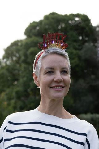 Smiling mature woman wearing merry christmas led headband in striped sweater outdoors