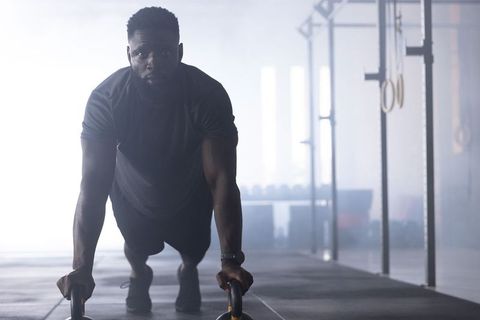 African american athlete performing parallette push-ups in backlit crossfit gym