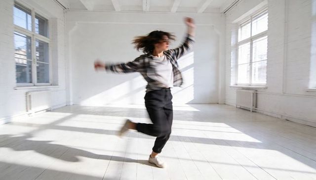 Young dancer spinning in sunlit minimalist studio wearing plaid shirt and sneakers