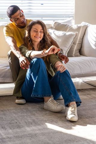 Sunlit african american man and woman sitting on carpet while woman showing smartwatch