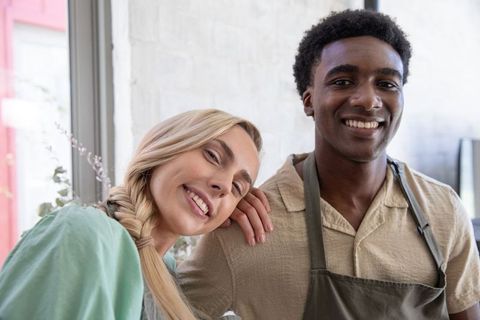 Smiling café coworkers wearing aprons standing by window