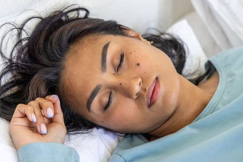 Resting asian woman lying on bed with pastel nails, serene closeup, minimalist bedroom