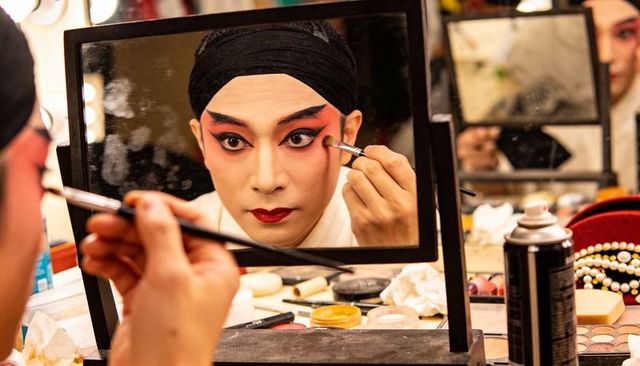 Backstage performer applying dramatic theatrical makeup in mirror before performance