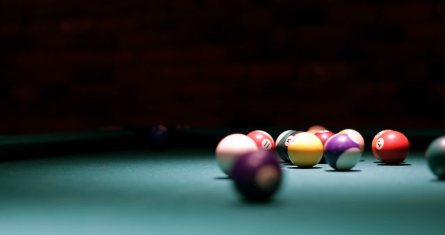 Colorful billiard balls on green pool table with dim lighting in dark room. Ideal for use in articles or designs related to sports, cue sports, entertainment, recreational activities, nightlife culture, bars, and pubs.