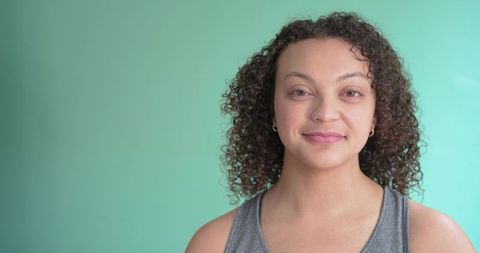 Confident young woman with curly hair smiling against teal backdrop for wellness branding