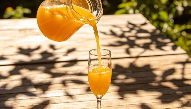 Pouring fresh orange juice from pitcher into stemmed glass on sunlit wooden patio table
