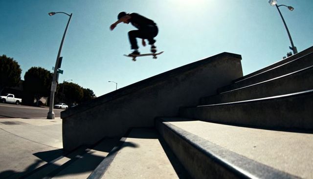 Skateboarder Ollie Jumping Over Concrete Stair Ledge Under Bright Blue Sky