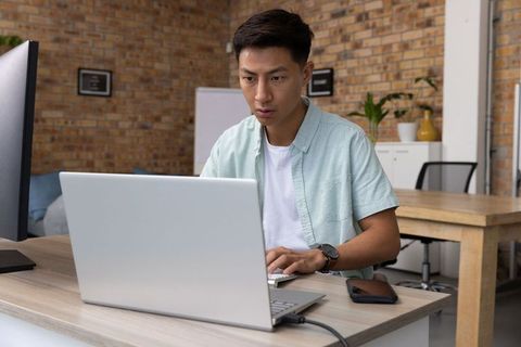 Focused Young Asian Man Working on Laptop in Modern Loft