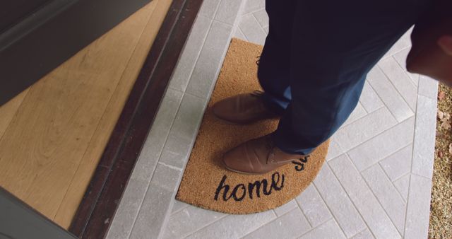 Person wearing brown shoes is standing on a welcome mat with 'home' text at a doorway. Suitable for use in hospitality, home selling, real estate marketing, blog and article images on home comfort, and lifestyle websites.