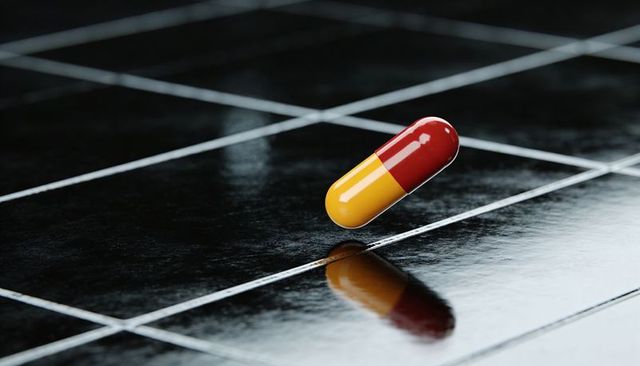Red-Yellow Capsule Resting on Glossy Black Tile Grid Reflecting Pharmaceutical Concept