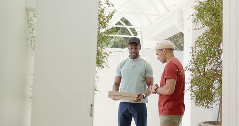 Courier handing takeout box while recipient checking wristwatch on sunlit porch