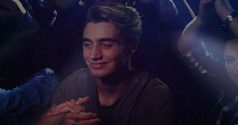 Young man leaning on barrier smiling at live concert in crowded nightclub with colorful lights