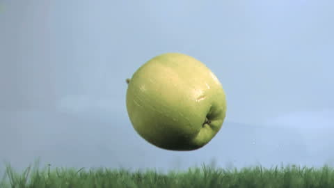 Green Apple Falling on Grass Against Blue Sky in Slow Motion