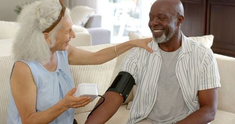 Elderly couple using digital blood pressure monitor indoors