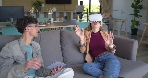 Young professionals testing VR headset on office sofa for collaborative startup innovation