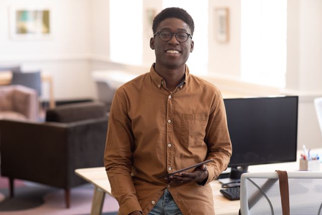 Portrait of happy African American professional businessman working in a modern creative office, wearing glasses and looking at camera smiling, holding a digital tablet. Business office creativity.