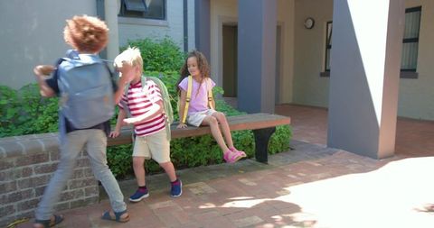 Back to school kids leaving courtyard bench with backpacks on sunny afternoon