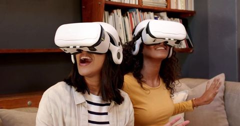 Excited female friends immersed in virtual reality at home