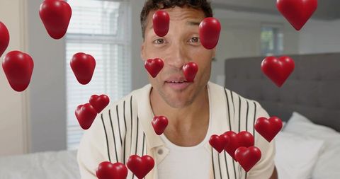 Mid-adult man sitting on bed surrounded by floating 3d hearts augmented reality love portrait