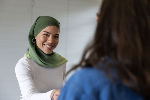 Smiling businesswoman in green hijab shaking hands with colleague in office meeting