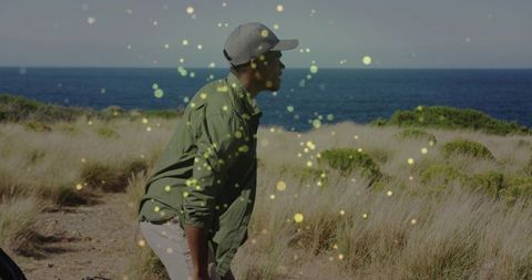 Contemplative man leaning on coastal path gazing at ocean with golden bokeh sunlight