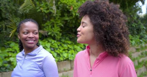 Friends walking and talking on garden path wearing quarter-zip active tops, smiling