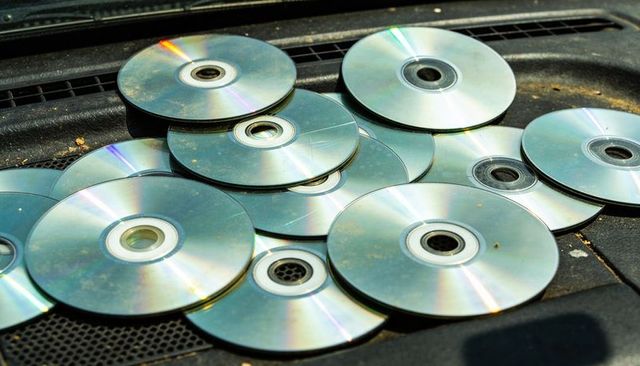 Glinting pile of optical discs scattering rainbow light across dusty car dashboard vent