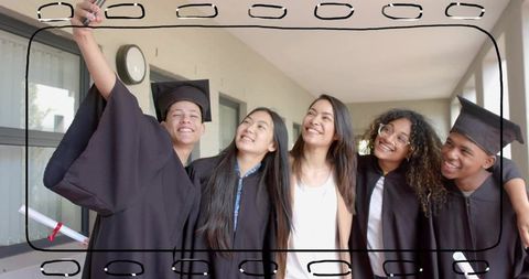 Graduates celebrating together while taking selfie in cap and gown on campus corridor
