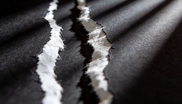 Torn black paper revealing white core under dramatic diagonal light and textured fibers