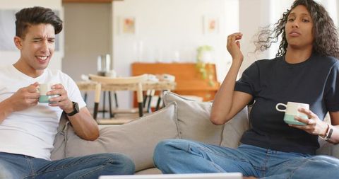 African American couple sharing coffee on sofa with playful reaction in cozy living room