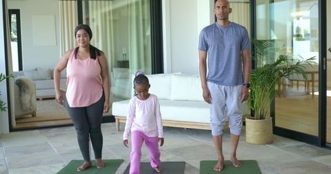 Family practicing yoga together on mats in bright living room near glass doors for wellness