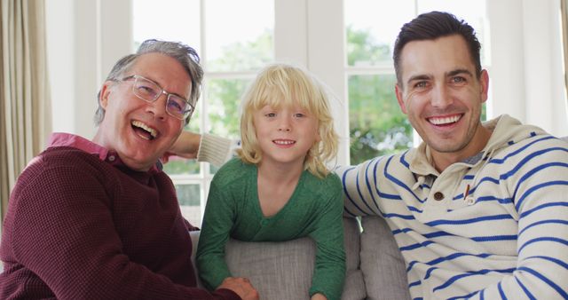 Three generations of family members sitting on a couch and smiling at the camera. Perfect for depicting family bonds, home life, and multi-generational relationships in promotional materials, advertisements, and family-oriented content.