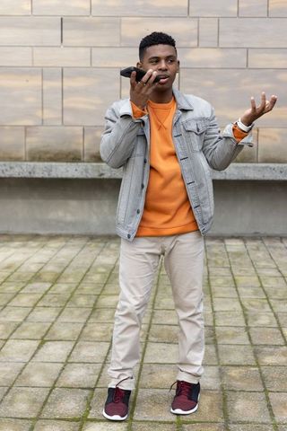 Young african american man speaking into smartphone and gesturing in urban courtyard