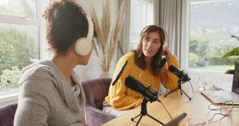 Two women recording podcast at home studio wearing headphones and using microphones