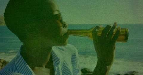 Sunlit seaside portrait of woman drinking from bottle in sunglasses and striped shirt