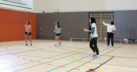 Diverse women practicing indoor volleyball drills in gymnasium during daytime training