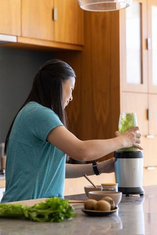 African american woman blending green smoothie at modern kitchen island for daily wellness