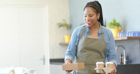 Smiling African American Barista Delivering Takeout Coffee and Box in Modern Cafe