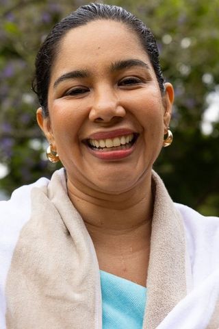 Warm smiling woman wearing gold hoop earrings and beige scarf in outdoor garden portrait